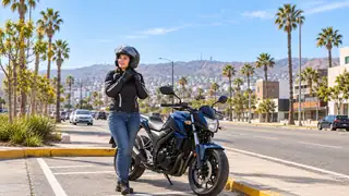 Motociclista con casco junto a su moto estacionada en una calle ilustrativa de Baja California.